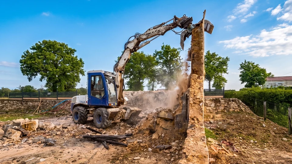 Chantier de démolition en extérieur avec pelleteuse hydraulique équipée d'un godet-pince démolissant une maison résidentielle