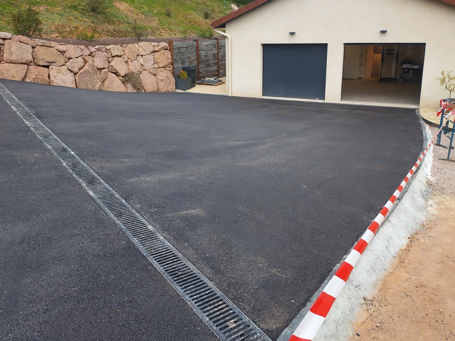 Rue résidentielle avec revêtement d'asphalte fraîchement posé, bordée de maisons unifamiliales avec garages et jardins paysagers